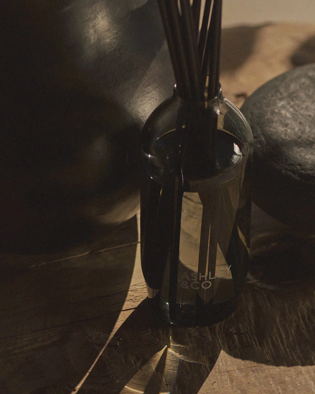 Ashley & Co Tui & Kahili Home Perfume Reed Diffuser among black table accessories and long shadows