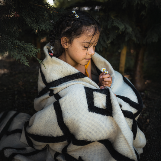 A photo of a child wrapped in the Diamante Black & White Tonal Blanket, highlighting the lighter side of the blanket. Perfect for indoor and outdoor use.