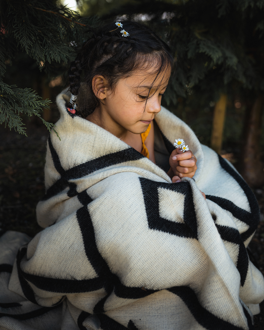A photo of a child wrapped in the Diamante Black & White Tonal Blanket, highlighting the lighter side of the blanket. Perfect for indoor and outdoor use.