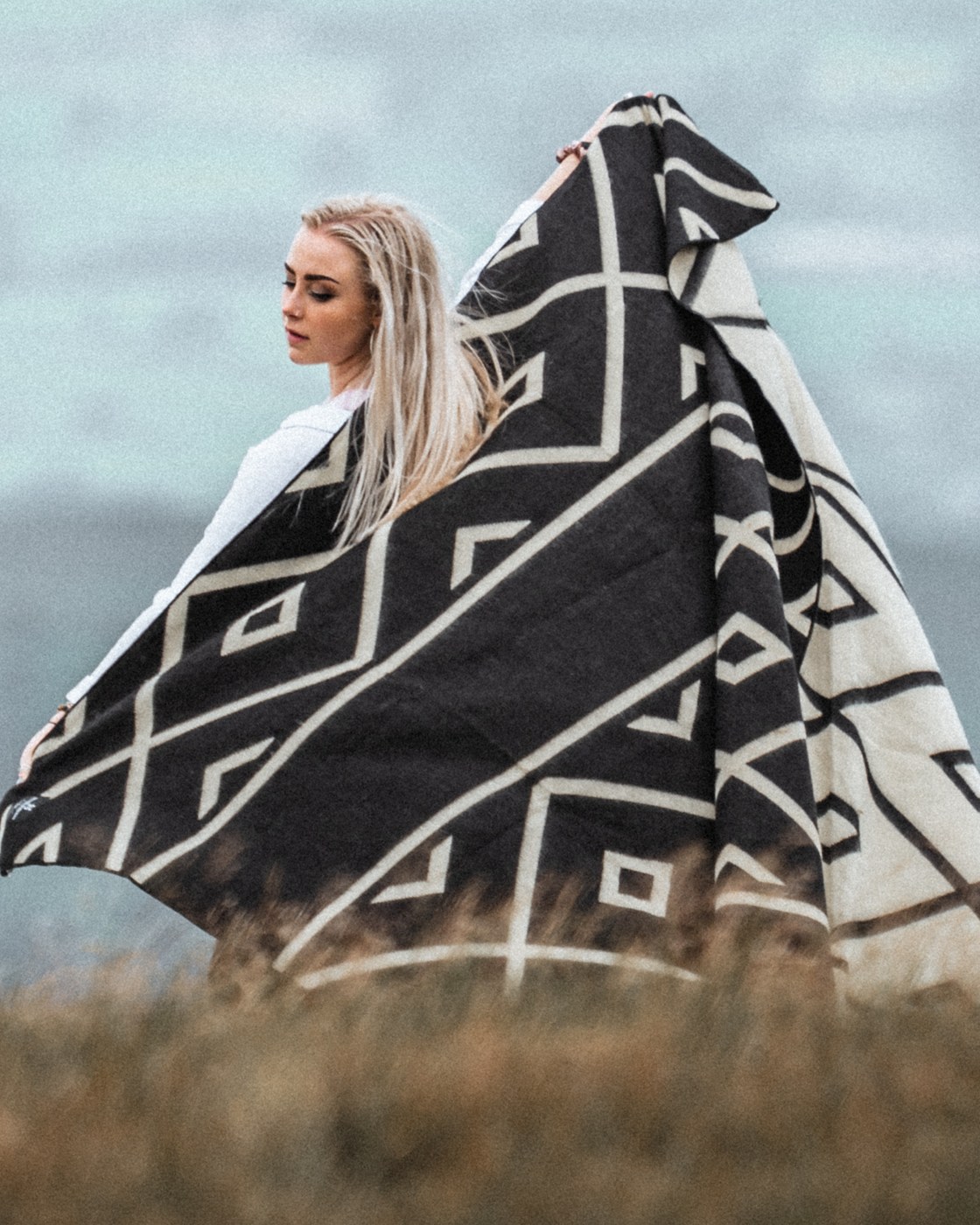 Gifts for the Hard-to-Buy-For: A lady holding up the Beyond Borders Diamante Black & White Tonal Blanket, giving you an idea of scale and the two tone design being light on one side and dark on the other.
