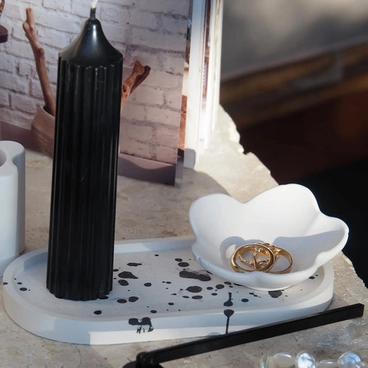 White flower-shaped trinket bowl jewellery holder with gold rings inside placed on bedside table.