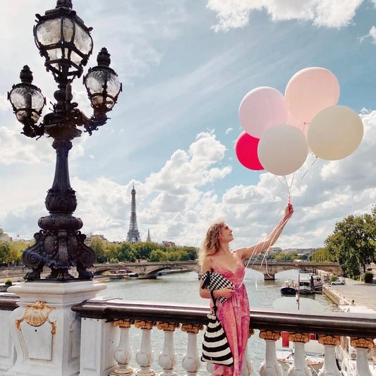 Large handprinted fabric gift bag in black and white stripes hung of the wrist of a woman on a Parisian bridge. Lush.