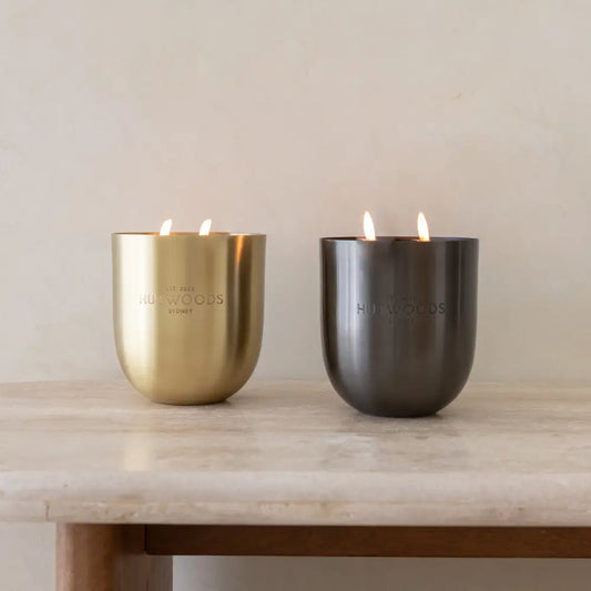 Two large Hutwoods candles in gold and black on a marble table