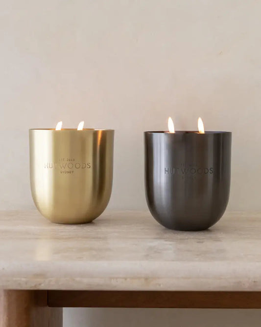 Two large Hutwoods candles in gold and black on a marble table