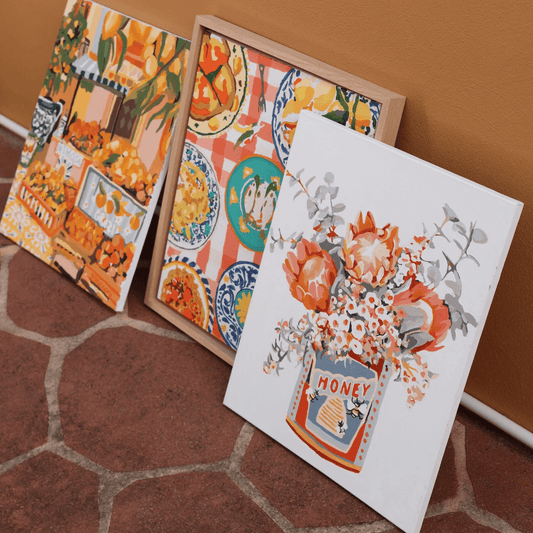 A collection of paintings leaning against a wall including Nonna's House framed and ready to hang.