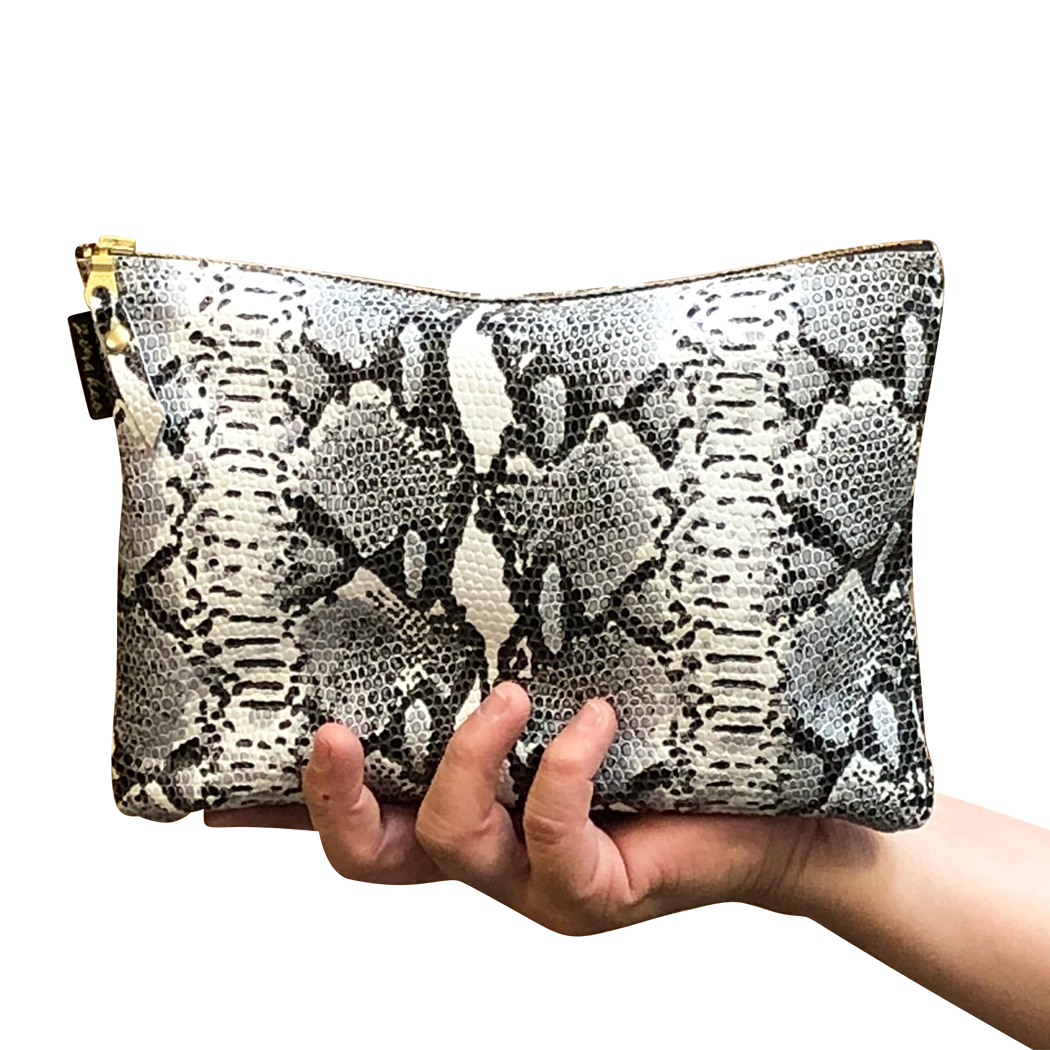 A hand holding a snakeskin leather travel pouch with a gold-toned zipper.