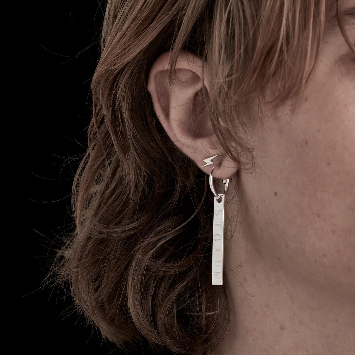 A close up of a model wearing Stolen Girlfriends Club's Silver I’ll Be Lightning Earring in a stack to give you a sense of scale. They're so stinking cute!