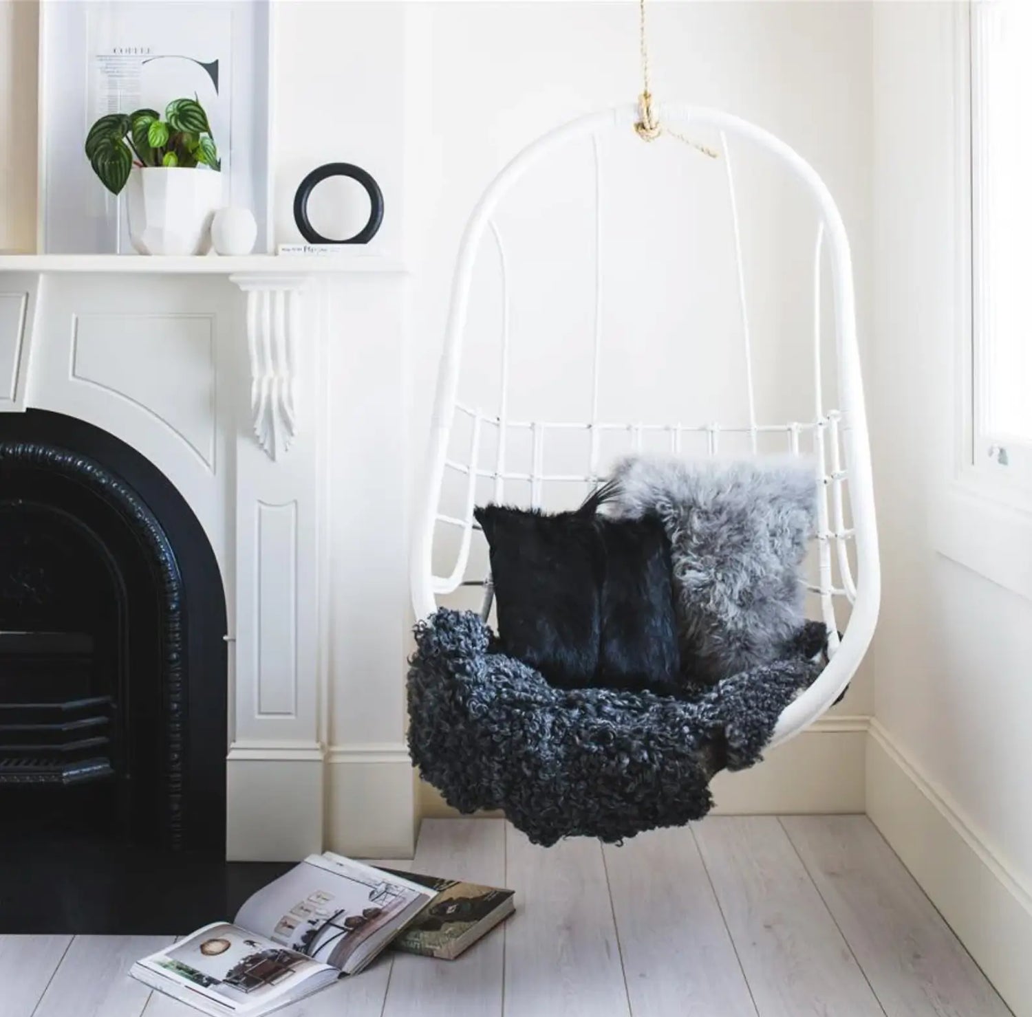 Hanging chair with sheepskin cushions and throw in a room with a cosy fireplace.