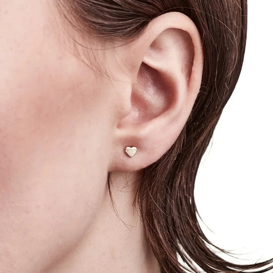 A model wearing the Stolen Girlfriends Club Tiny Stolen Heart Earrings in gold. They are gold plated sterling silver and so well made.