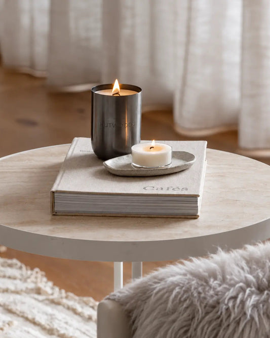 Scandi lounge setting with xl metal vessel candle on light table with book, light furnishing.