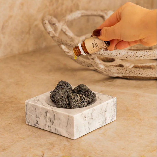 Hand holding a bottle of Alta Balance essential oil above the Marble Incense Holder with Lava Stones.
