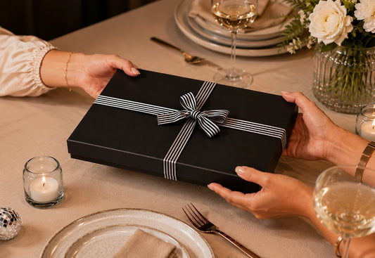 Woman handing a luxury black gift box across a decorated birthday table with flowers, candles and disco balls, perfect for unique gifts for women in Australia.