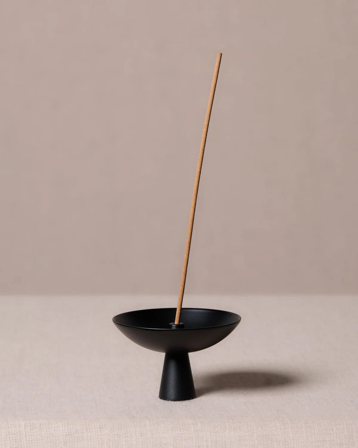 Alta Saturn Nickel incense holder in a black finish with a single incense stick, featuring a minimalist pedestal design for catching ash during burning.