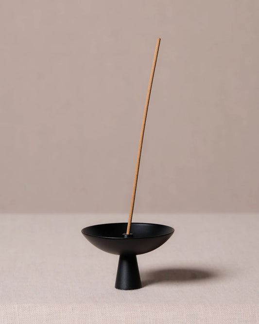 Alta Saturn Nickel incense holder in a black finish with a single incense stick, featuring a minimalist pedestal design for catching ash during burning.