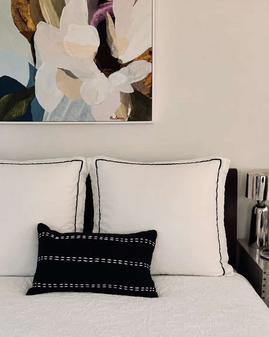 Black raw linen lumbar cushion with white hand-stitched detailing styled on a contemporary monochrome bed.