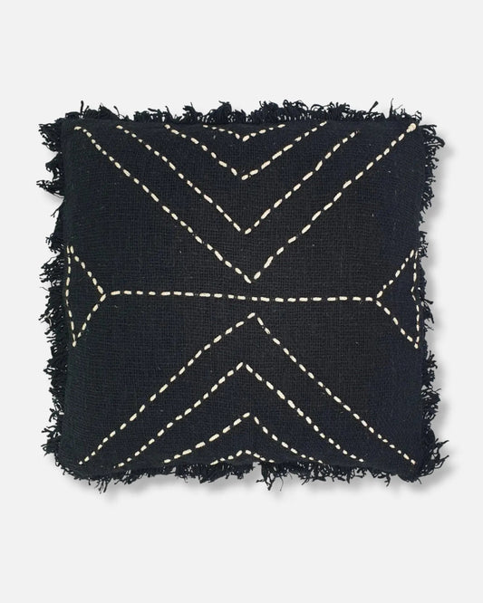 A square black throw pillow with frayed edges and cream-colored geometric stitched patterns, shown against a light gray background.