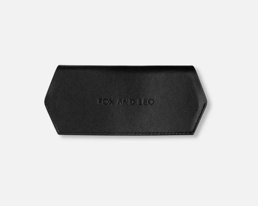 A black leather eyeglasses case with a hexagonal shape, featuring the debossed brand name 'FOX AND LEO' in the center, set against a light gray background.