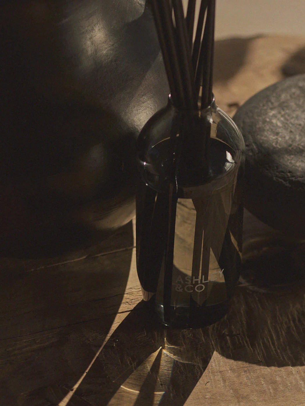 Ashley & Co Tui & Kahili Home Perfume Reed Diffuser among black table accessories and long shadows