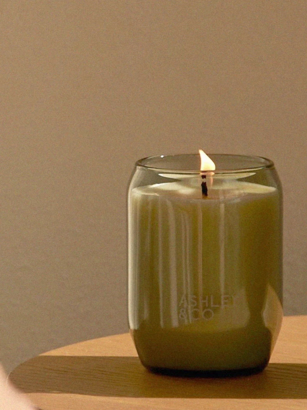Ashley & Co Parakeets & Pearls Waxed Perfume Candle burning under long shadows on a wooden table