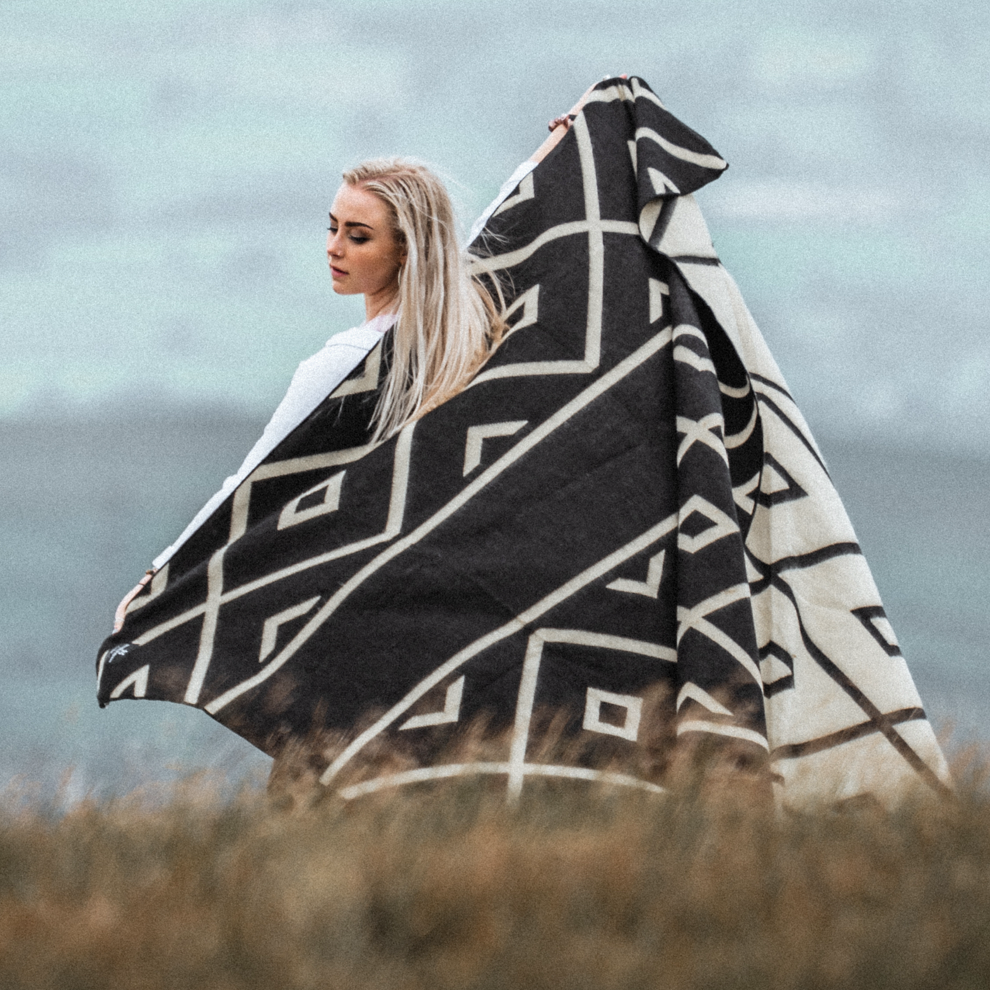 A lady holding up the Beyond Borders Diamante Black & White Tonal Blanket, giving you an idea of scale and the two tone design being light on one side and dark on the other. 