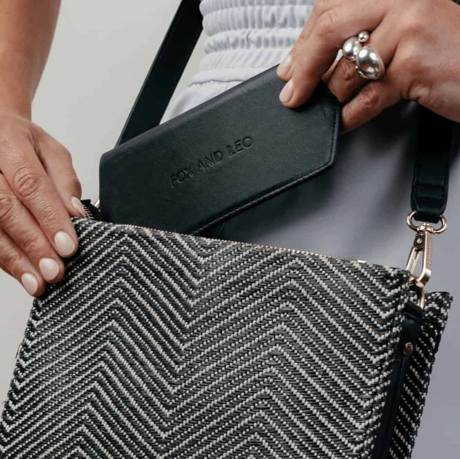 Person putting their Fox and Leo glasses case in black in their handbag. It's so small it fits in almost any bag!