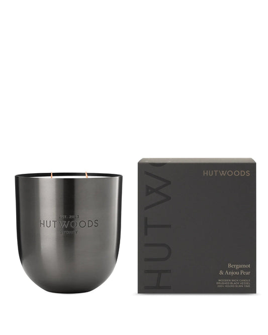 A lit Hutwoods Bergamot & Anjou Pear Candle in brushed black vessel on a white background