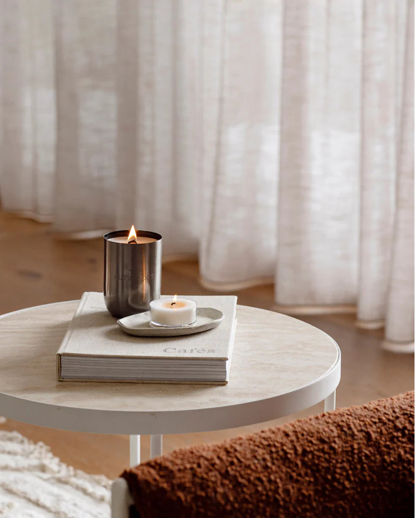 A Hutwood 80 hour candle in a gunmetal grey metal container burning on a coffee table in a calm and elegant lounge room.