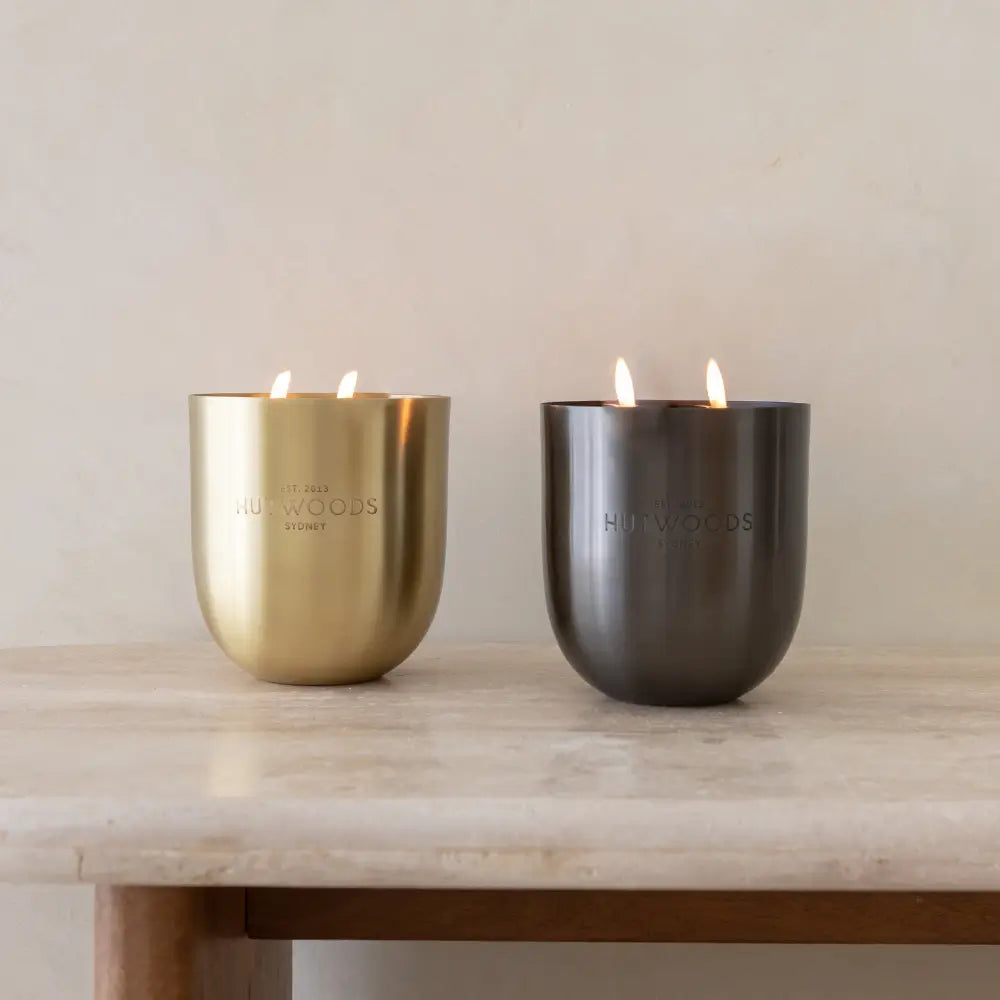 Two large Hutwoods candles in gold and black on a marble table 