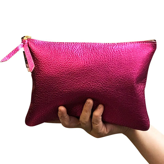 A hand holding a metallic fuchsia leather pouch with a gold zipper.