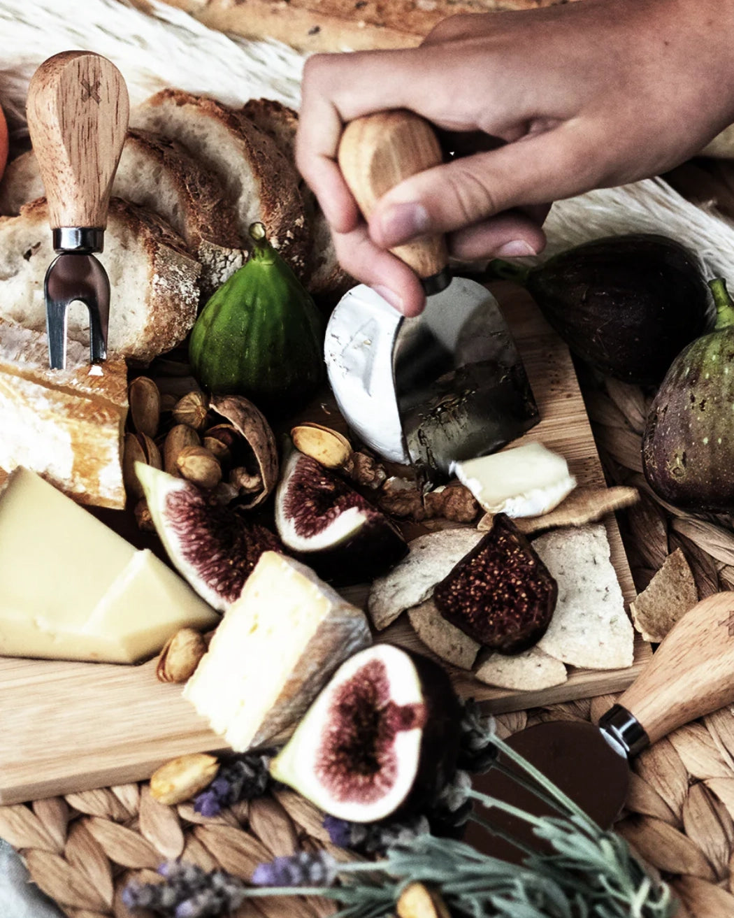 The Peli "Feta Together' Cheeseboard with figs, cheese, bread, and nuts on a woven surface. Looks yum.