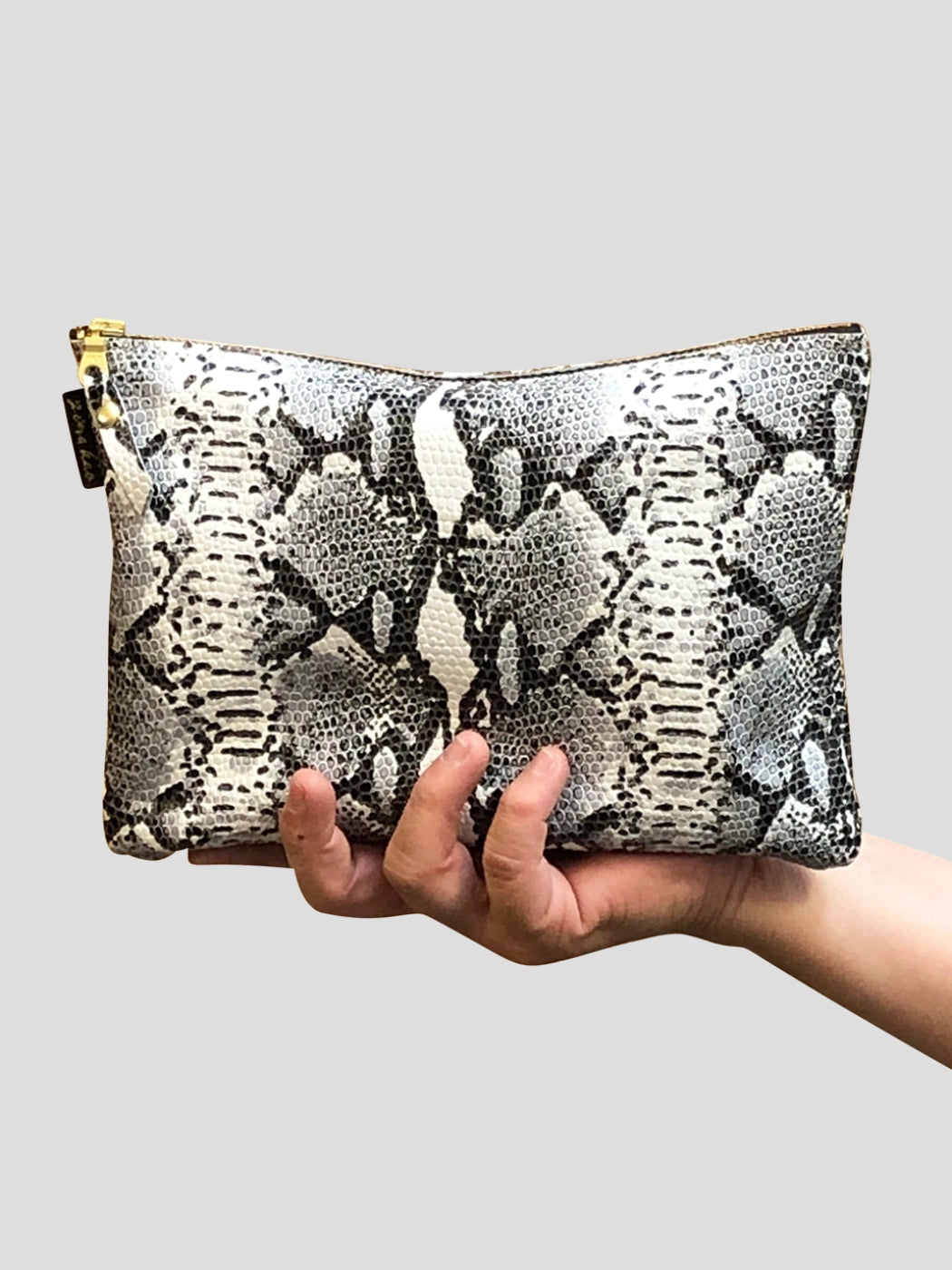 A gorgeous snakeskin leather pouch being held in someones hand on a grey background.