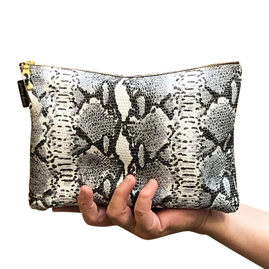 A hand holding a snakeskin leather travel pouch with a gold-toned zipper.