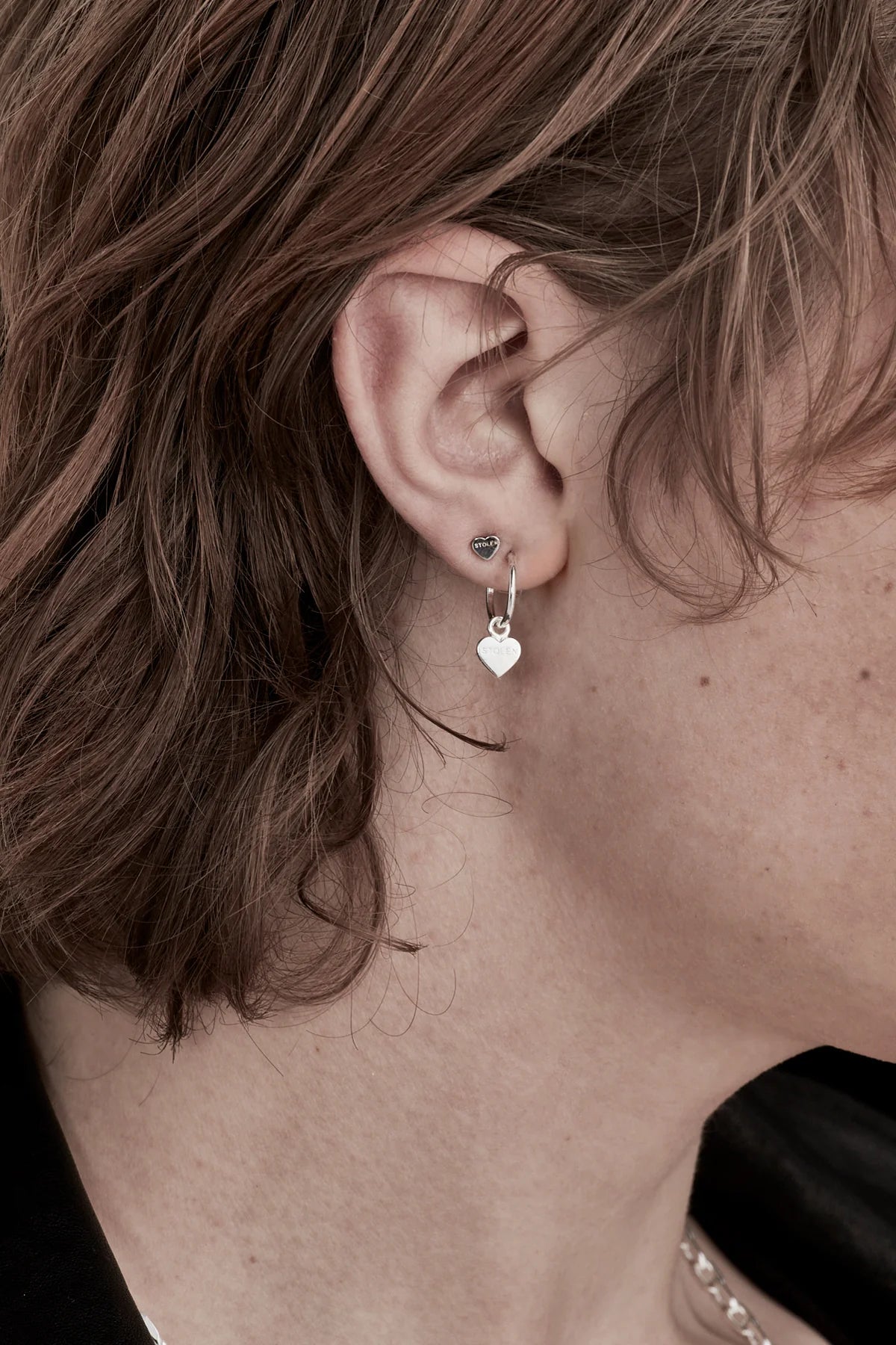 A close up of a model wearing the Stolen Girlfriends Silver Tiny Stolen Heart Earrings to give you a sense of scale. They're small but they're gorgeous and great for stacking.