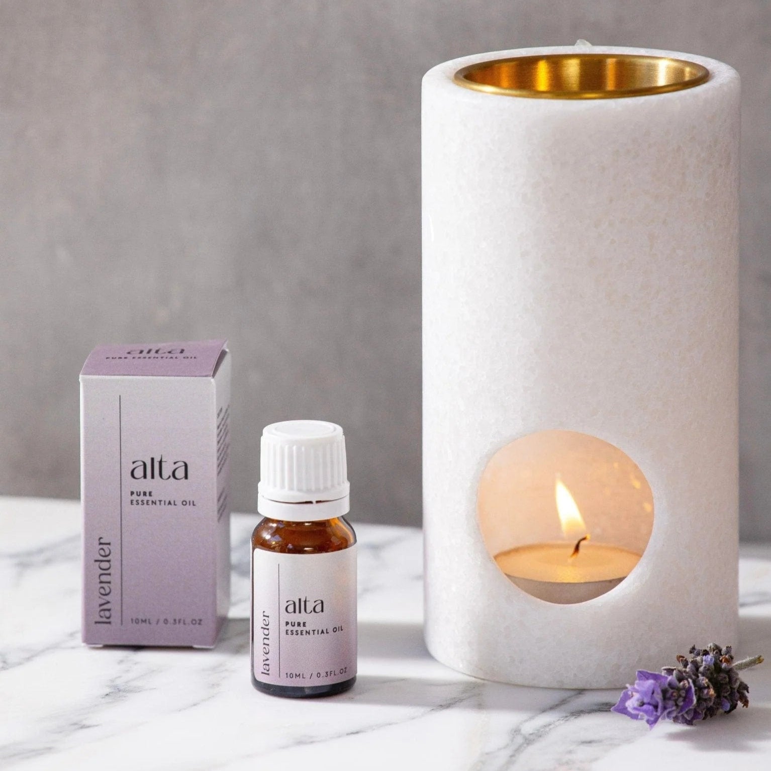 Alta lavender essential oil bottle and packaging with a candle in the background on a marble surface.