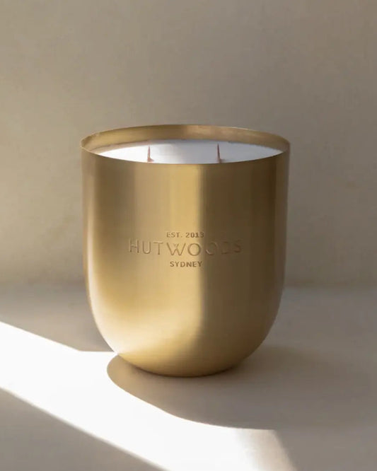 Large Brass Metal candle sitting in filtered sunlight agains minimalist background