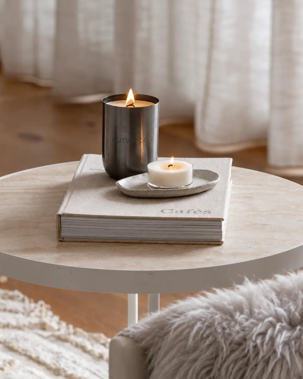 Scandi lounge setting with xl metal vessel candle on light table with book, light furnishing. 