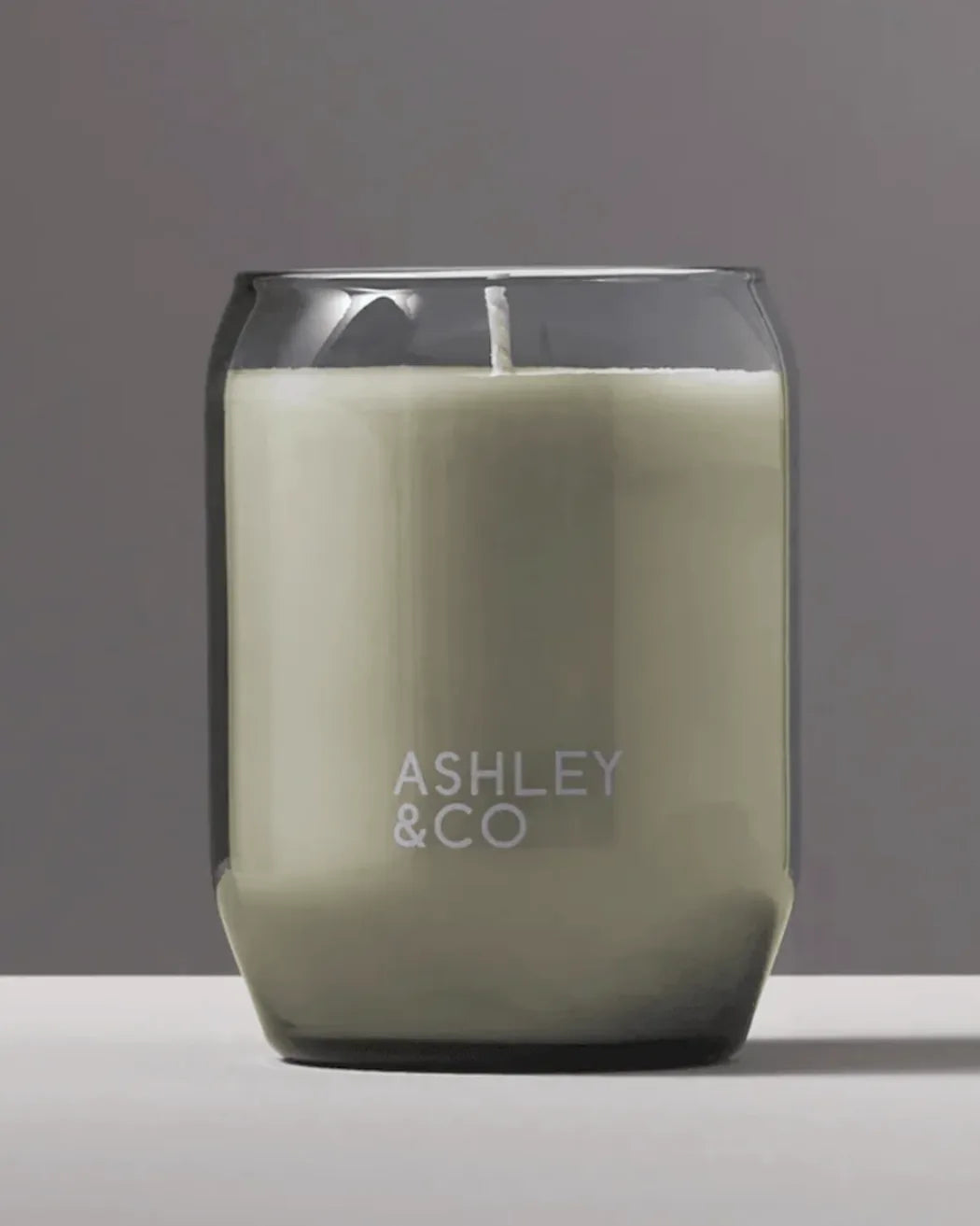 Ashley & Co Blossom & Gilt waxed perfume candle 310g in a smoky grey hand-blown glass vessel on a soft grey studio background