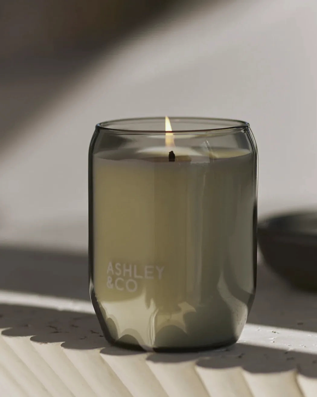 Lit Ashley & Co Blossom & Gilt scented candle in smoky glass, glowing in warm natural light with soft shadows