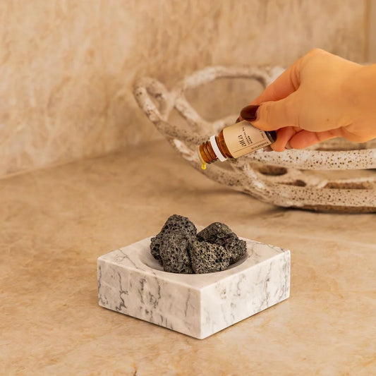 Hand holding a bottle of Alta Balance essential oil above the Marble Incense Holder with Lava Stones.