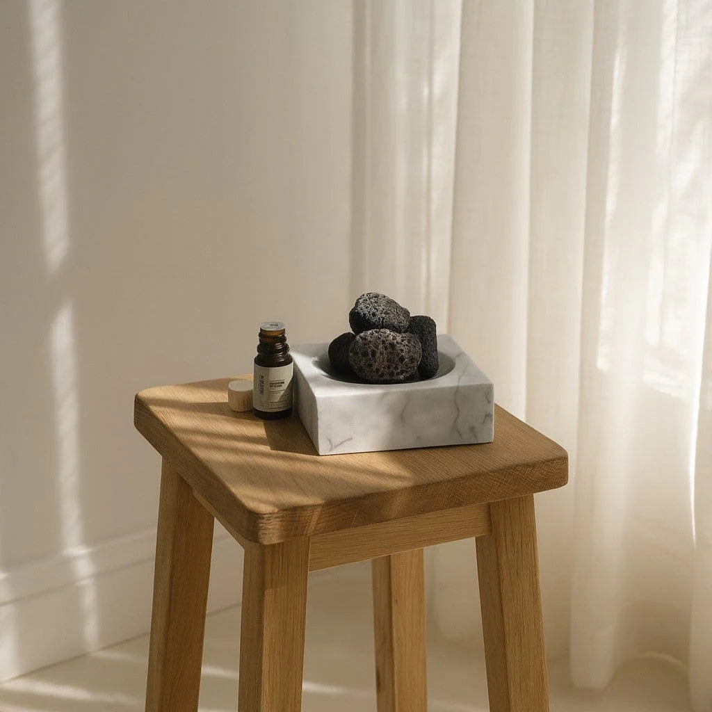 Small wooden table with the Marble Incense Holder with Lava Stones and a bottle of Alta essential oils. A very serene scene. 