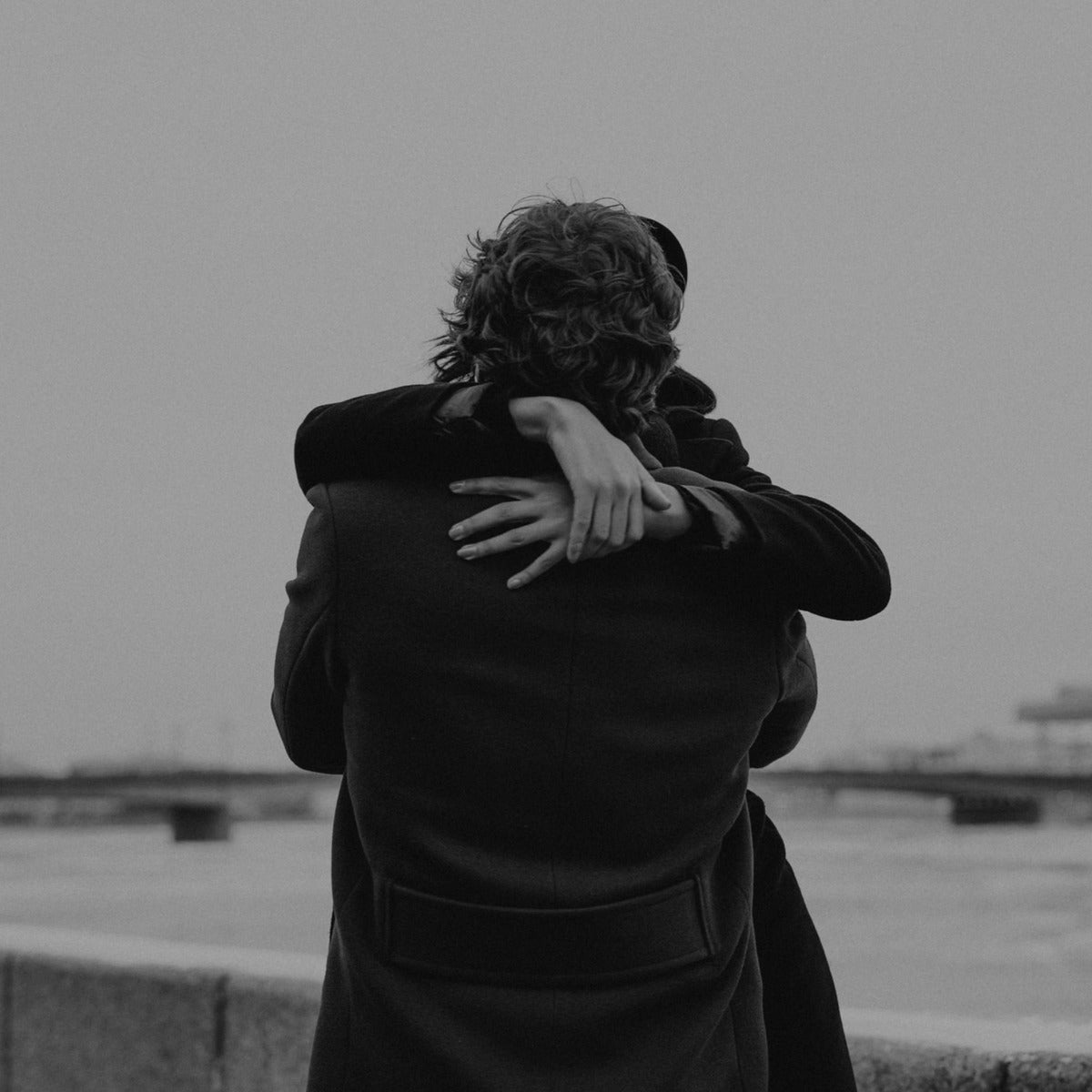 Two people sharing a warm thank you hug by the water, in black and white